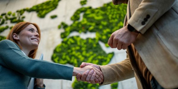 Two people shaking hands outdoors with a green world map background.