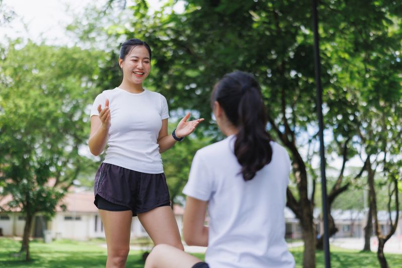 Young asian woman talking and gesturing to another woman in a park, discussing health, fitness, or personal training concepts