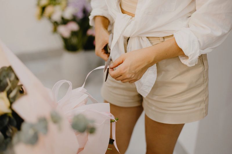 Florist cutting ribbon while preparing bouquet at counter.