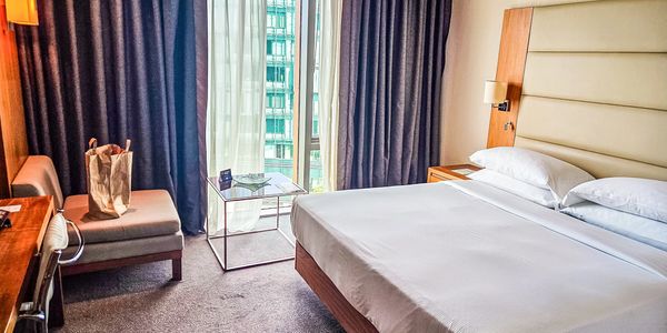 Modern hotel room with large bed and window.