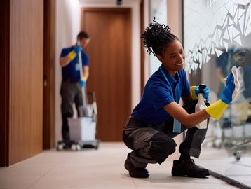 Two janitors cleaning glass in a hallway.
