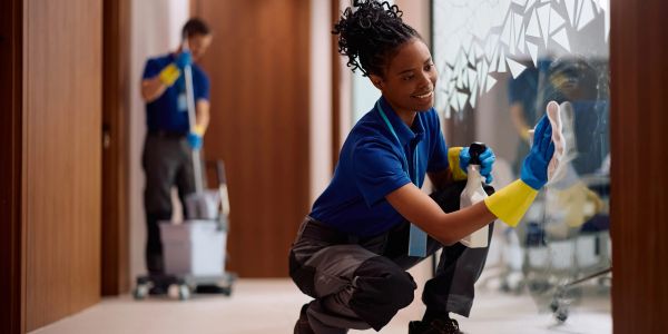 Two janitors cleaning glass walls and floors in a modern office hallway.