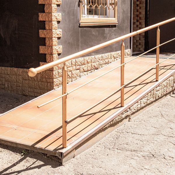A tiled wheelchair ramp with metal handrails beside a brick building.