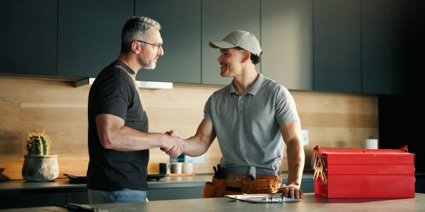 Man shaking hands with a repairman in a kitchen.