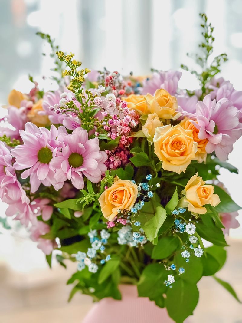 Colorful floral arrangement featuring fresh roses and daisies with green leaves in bright natural light suitable for wedding greeting cards and anniversary themes