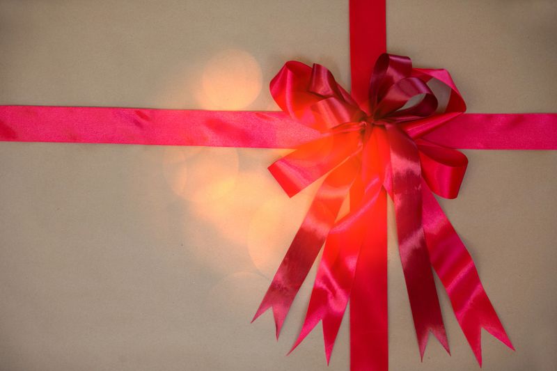 A beautifully wrapped gift features a bright pink ribbon and bow, set against a soft, blurred backdrop that adds a warm and celebratory atmosphere, perfect for special occasions.