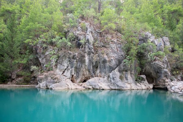 Turquoise water reflecting rocky cliffs and lush green trees.