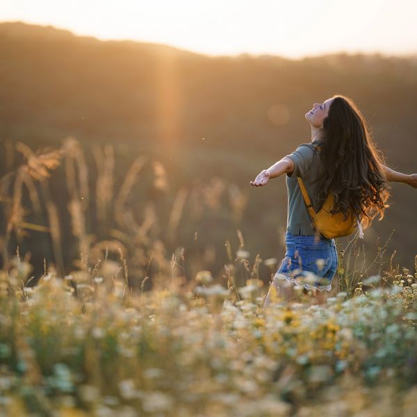 Woman with outstretched arms enjoying a sunny field of flowers at sunset.