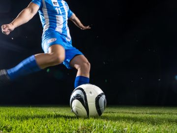 Soccer player kicking a ball on a grass field at night.
