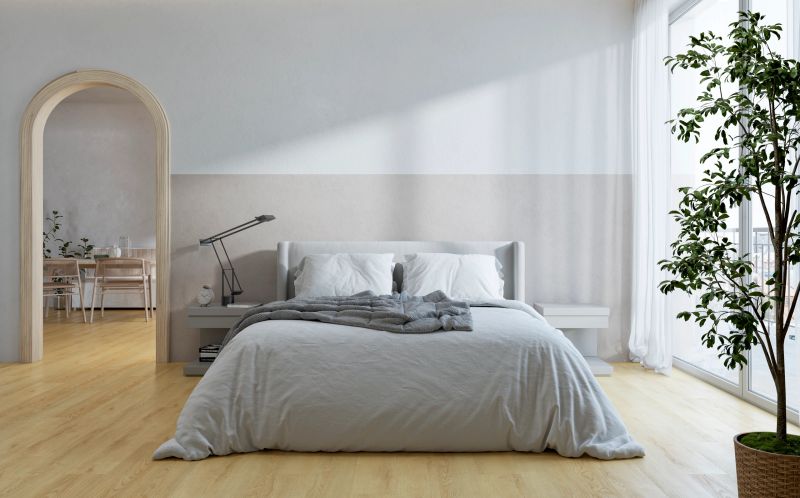 Bright contemporary bedroom interior with a low upholstered bed, soft neutral walls, light wood flooring, and abundant daylight from a floor-to-ceiling window with sheer curtains. The space features a minimalist design, an arched doorway, and a decorative indoor tree, creating a calm and elegant residential atmosphere. An arched doorway with dining room in background. A 3D rendered image.