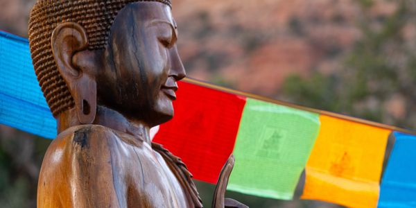 Wooden Buddha statue with colorful prayer flags in the background.