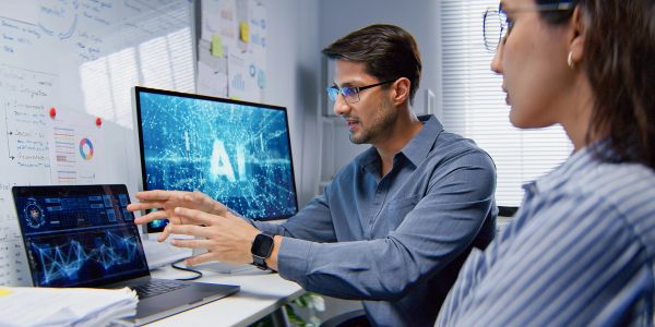 Two professionals discussing AI data on computer screens.