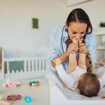 Mother playfully holding baby's feet on changing table.
