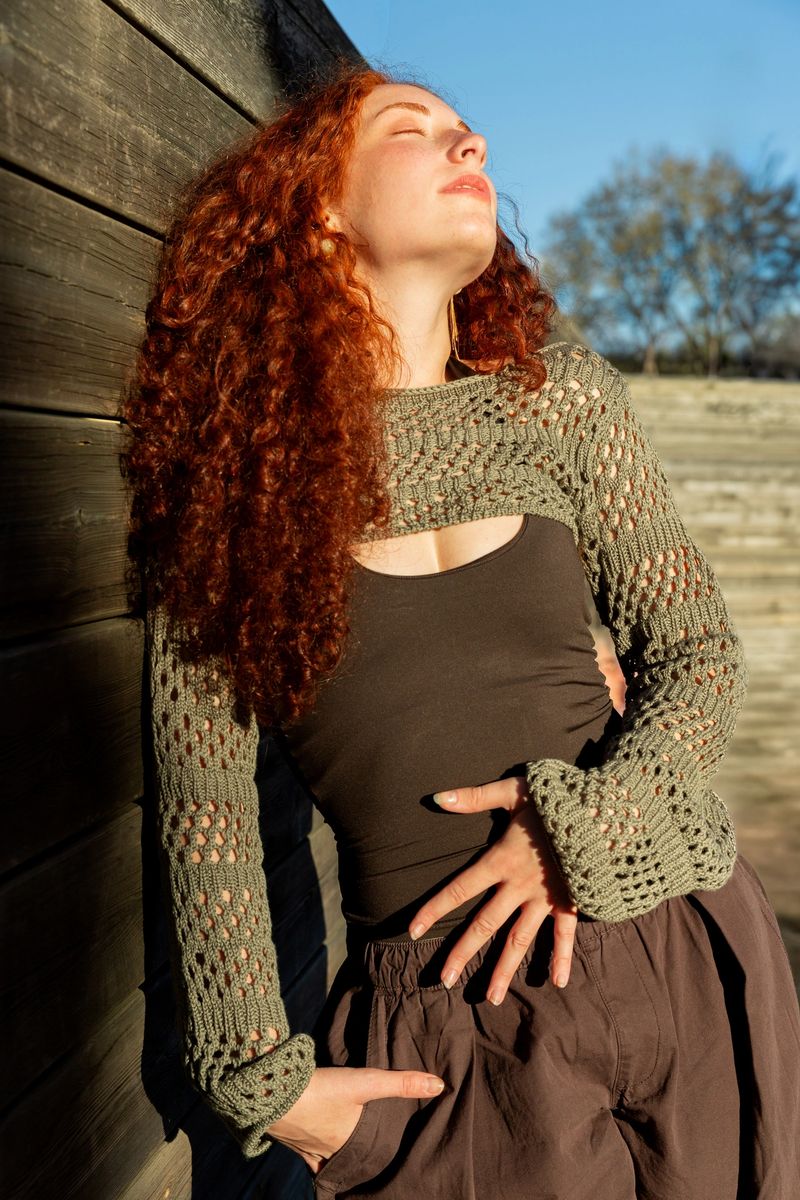 Woman with long curly red hair posing outdoors, enjoying warmth of sunshine on face