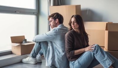 Couple sitting back to back among moving boxes.