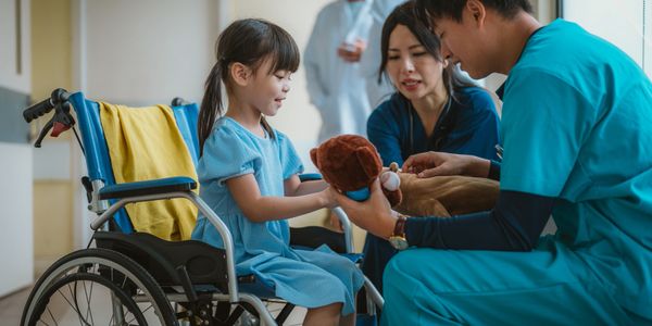 Healthcare professionals engaging with a young girl in a wheelchair using a stuffed toy.