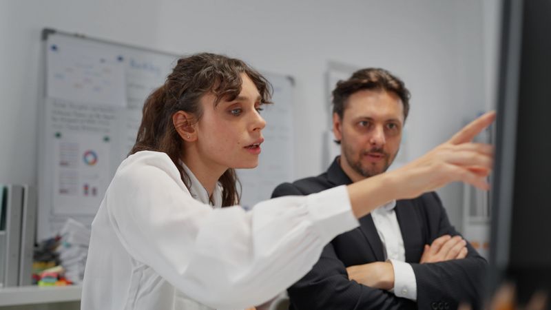 White woman business trainee consults a mentor during a one-on-one session in a modern office having discussion reviewing information marketing plan strategy  exemplifying teamwork collaboration