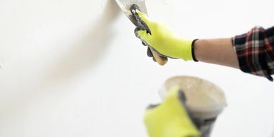 Person wearing yellow gloves applying plaster on a wall.