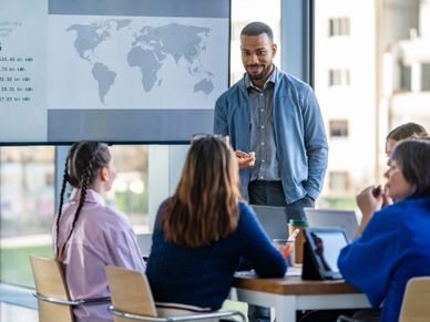 A man presenting a world map to a group in a meeting room.