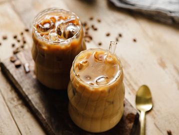 Two glasses of iced coffee on a wooden board.