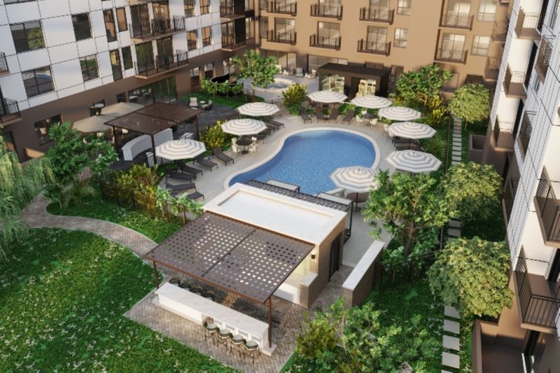 This image showcases an aerial view of a contemporary apartment complex featuring a swimming pool surrounded by lounge chairs and umbrellas. The landscaped garden includes pathways, greenery, and seating areas, creating a relaxing outdoor space for residents.