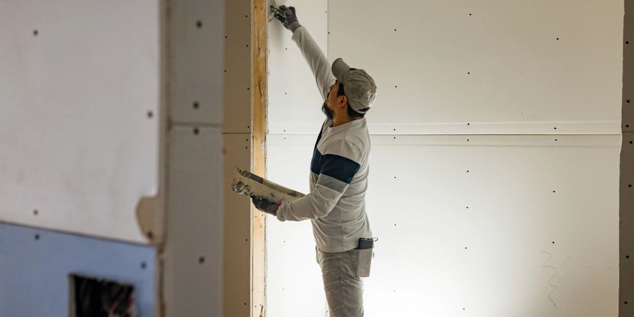 Drywall worker applying compound on wall and holes