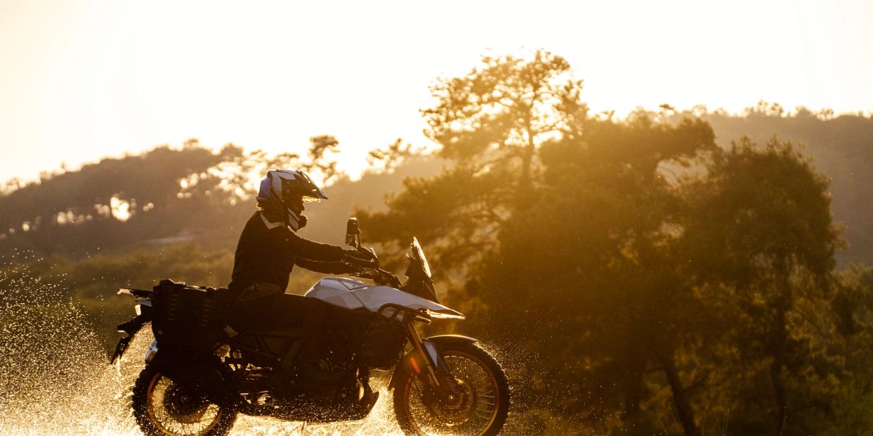Motorcyclist riding through water at sunset.