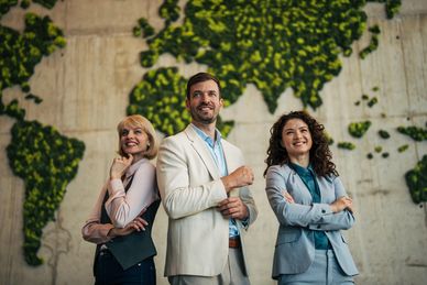 Three confident professionals standing with a world map behind them.