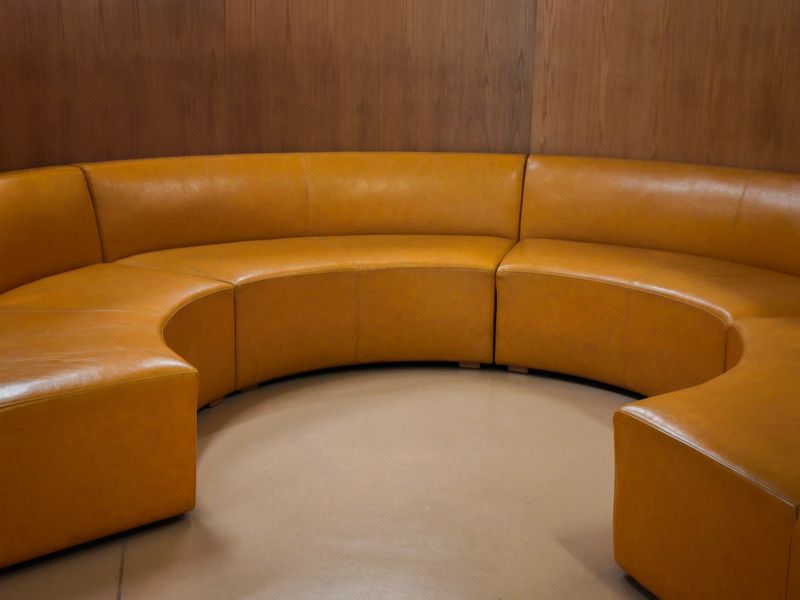 Curved tan leather sofa in modern interior. Mid-century modular seating, luxury furniture design concept.