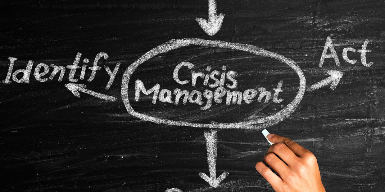 Hand writing 'Crisis Management' on blackboard with arrows to Identify and Act.