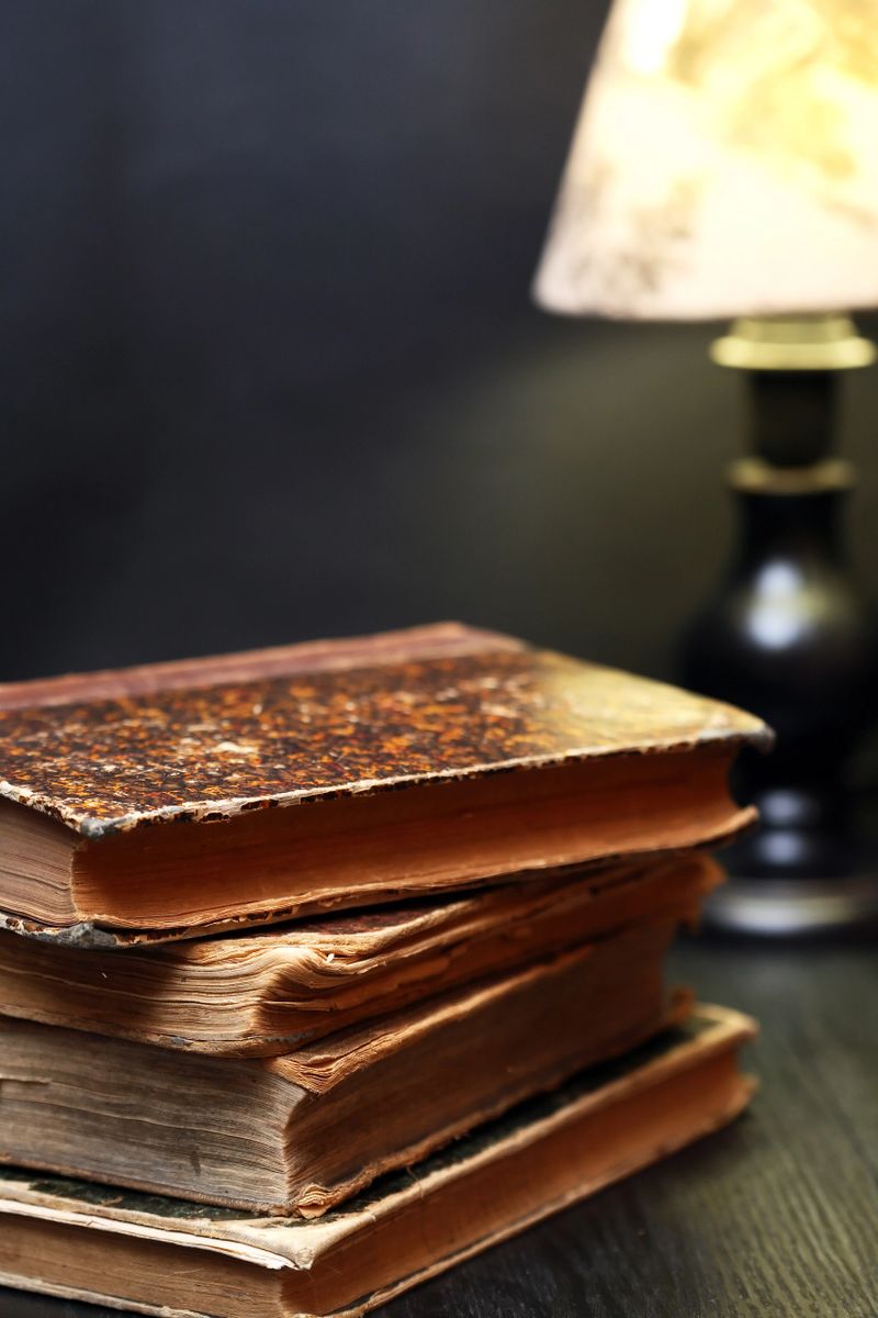 A set of old books with yellowed pages and various covers near lamp