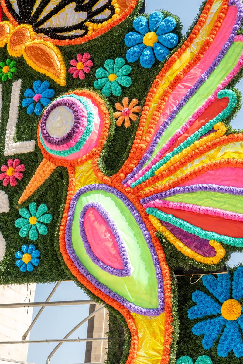 Vibrant artificial flowers forming a large hummingbird and floral patterns on an outdoor festival decoration