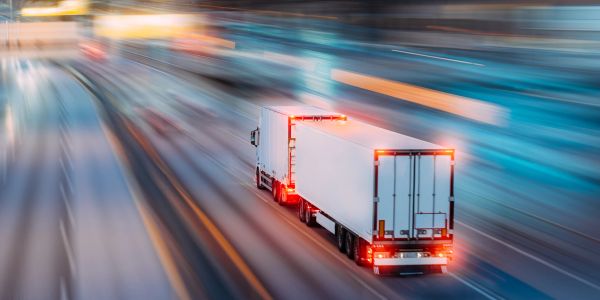 A semi truck driving fast on a highway at night.