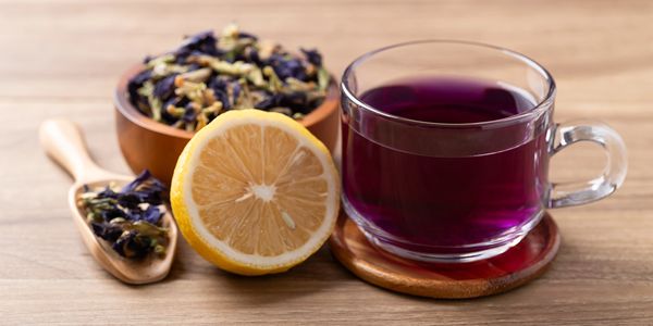 Cup of purple herbal tea with lemon and dried flowers.