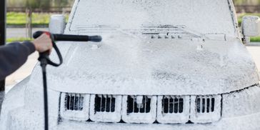 Person using foam cannon to wash a car.