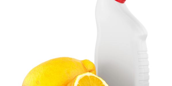 A lemon and a white plastic bottle with a red cap on a white background.