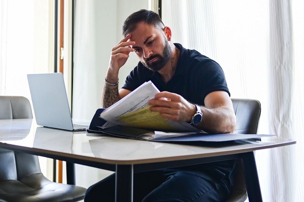 Man intensely reviewing documents at a table with a laptop.