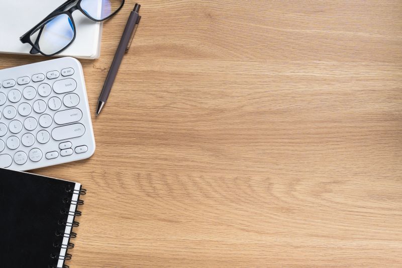 Elegant Workspace with Computer Keyboard, Notebook, Pen, Glasses, and Laptop on Light Wooden Desk for Creative or Office Use