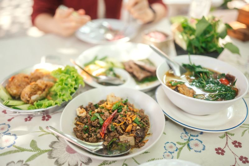 northern Thai culinary spread, featuring Lab Moo (spicy minced pork), Tom Khlong (spicy and sour herbal soup), and purple sticky rice. The arrangement highlights the diverse flavors and traditional herbal ingredients of the Lanna region.