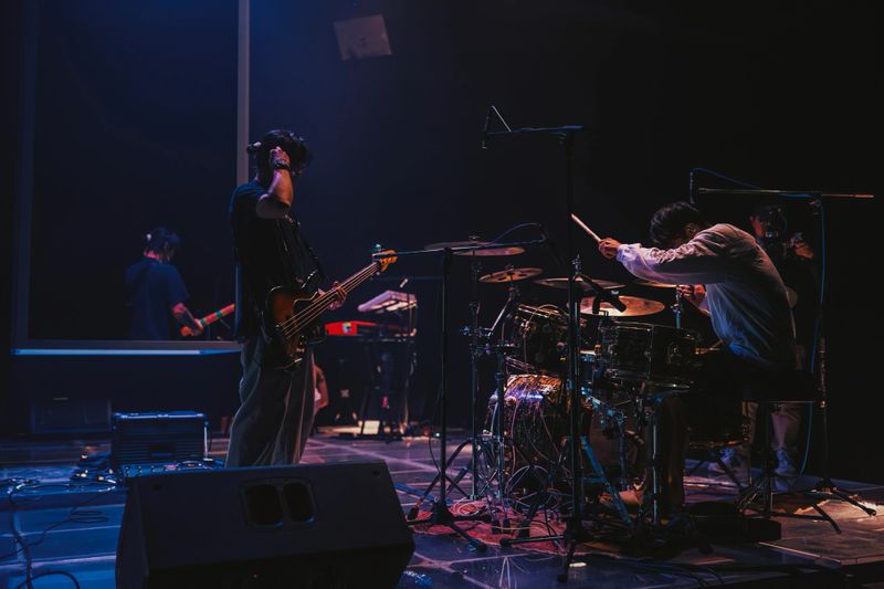 Asian musicians rehearse on stage during soundcheck with drums, bass guitar, and stage lighting before a live performance in Bangkok.