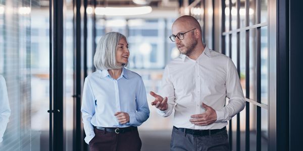 Two colleagues walking and talking in an office corridor.