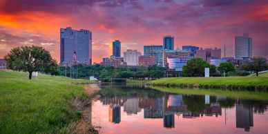 City skyline reflected in calm river during vibrant sunset.