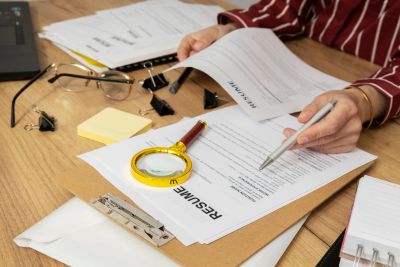 Person reviewing a resume with office supplies on a wooden desk.