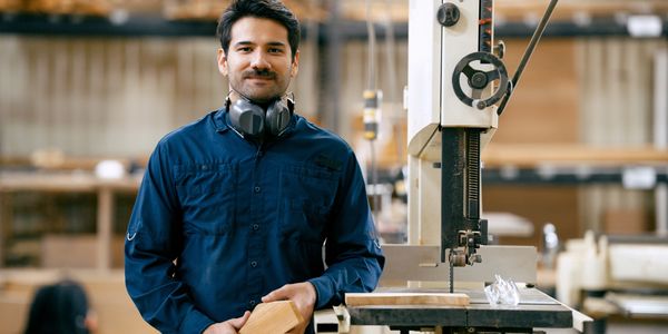 Small manufacturing shop owner standing confidently by his production equipment.