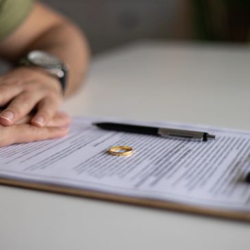 Anillo y documentos para divorcio con una persona al fondo.