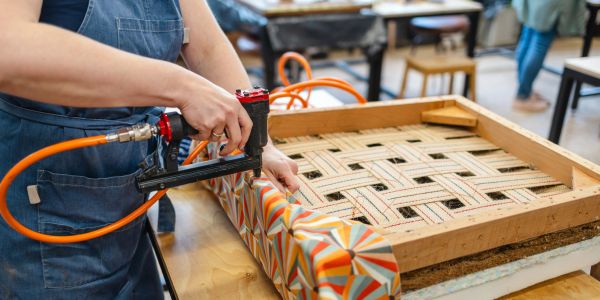 Person upholstering a chair with a staple gun.