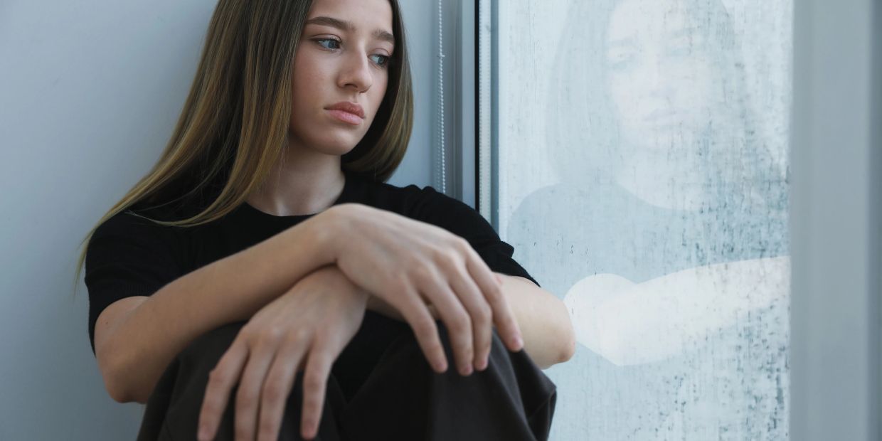 Sad woman sitting near a window, looking reflective.