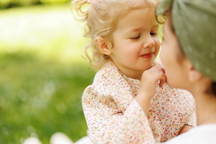 A mother gently holding her young daughter and looking into her eyes outdoors.
