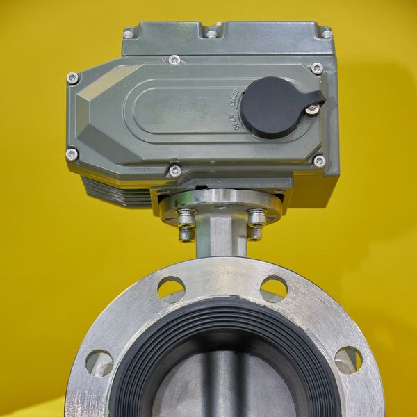 Metal industrial valve against yellow background.