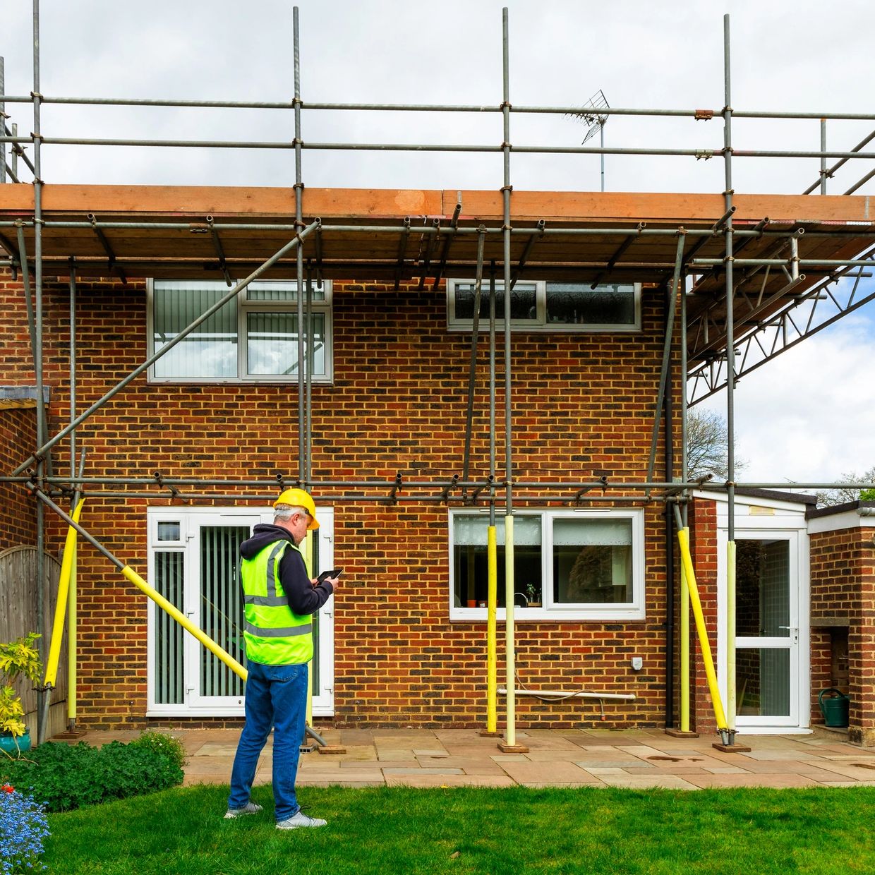 Construction worker inspecting a house with scaffolding.